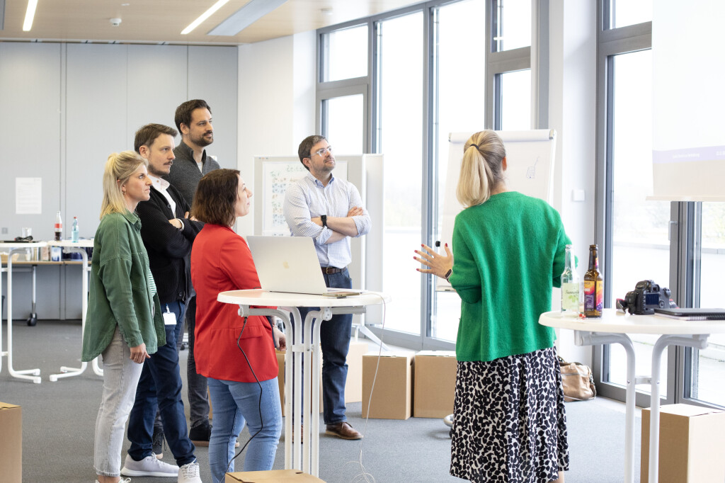 Präsentationstraining im Business-Kontext: Teilnehmergruppe verfolgt Flipchart-Präsentation einer Referentin im modernen Seminarraum.