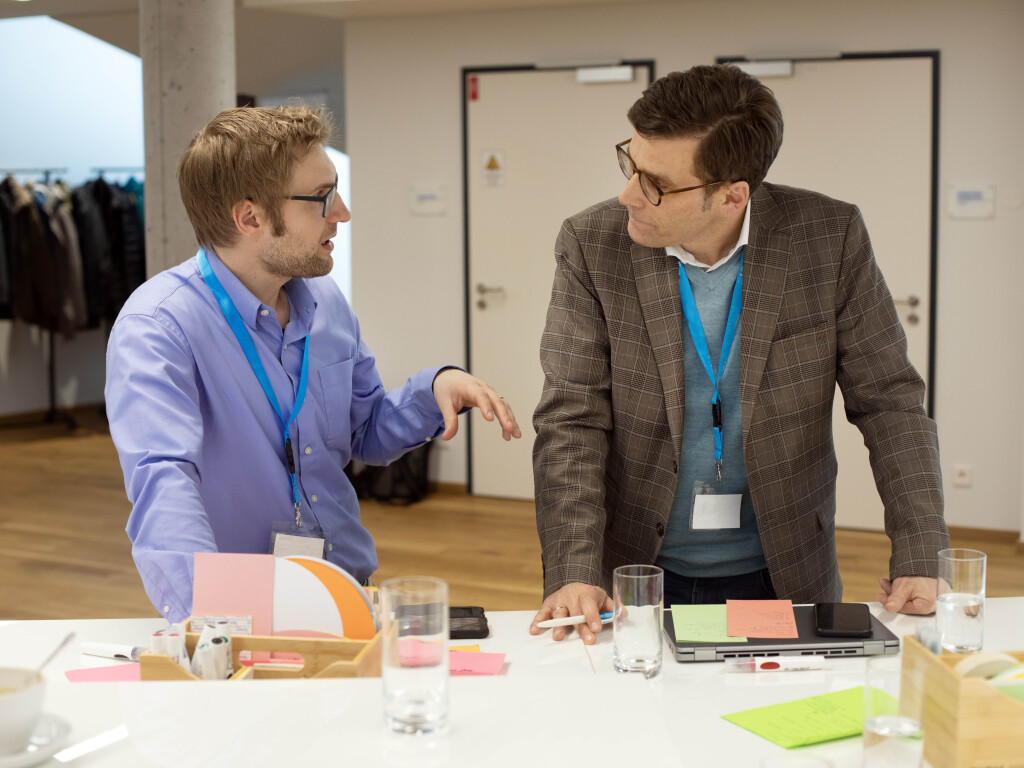 Zwei Teilnehmer im Führungstraining im intensiven Gespräch am Tisch mit Moderationsmaterialien.