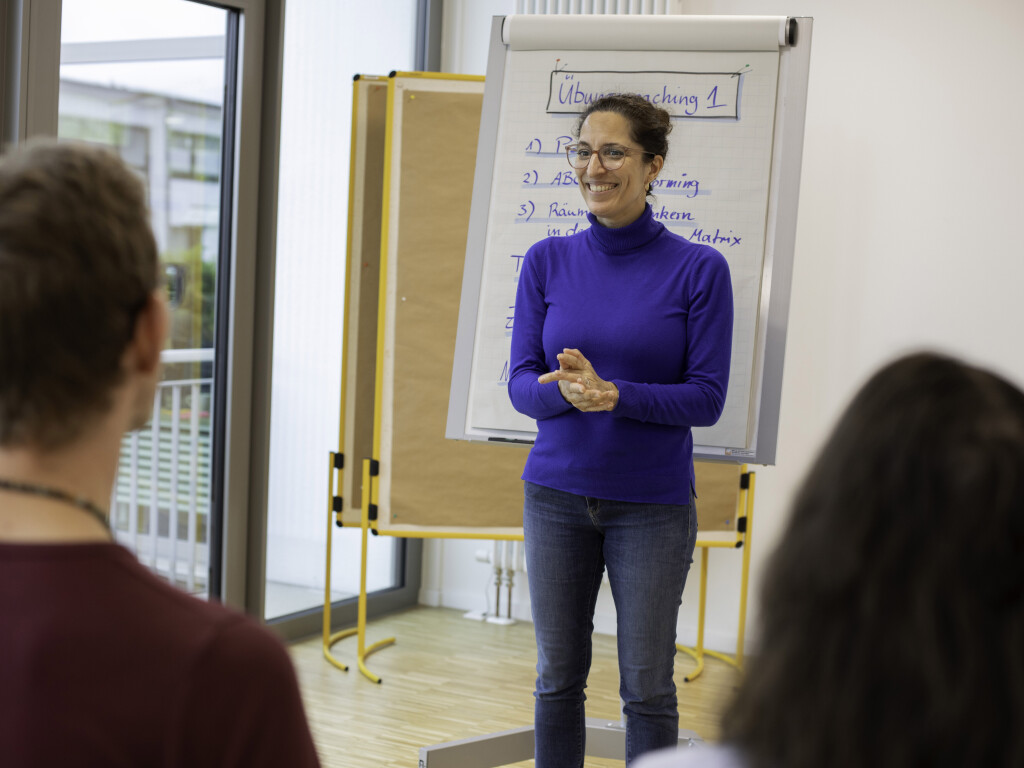 Trainerin leitet Moderationstraining vor Flipchart, Teilnehmende hören zu.