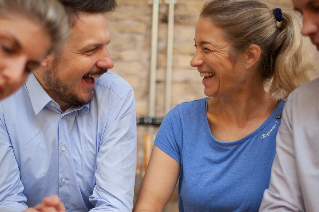 Mann und Frau sitzen nebeneinander, schauen sich an und lachen herzlich.
