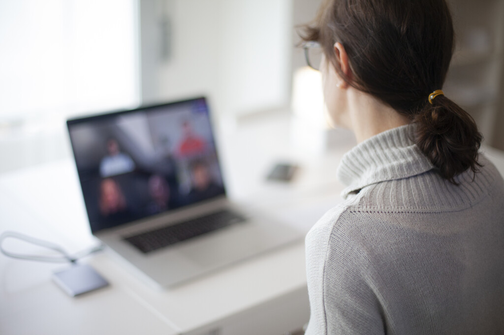 Frau mit Brille sitzt vor einem Laptop und nimmt an einem virtuellen Meeting mit mehreren Teilnehmenden teil – moderner Arbeitsplatz im Homeoffice.