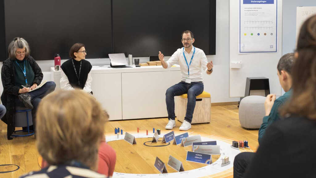 Trainer leitet einen Workshop im Sitzkreis mit Teilnehmenden, Moderationskarten und Coaching-Materialien – interaktives Training und Teamcoaching.