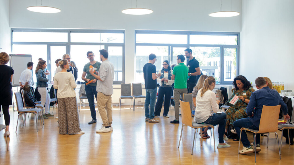 Workshop-Teilnehmende im offenen Austausch und Gruppenarbeit, verteilt im Raum stehend oder sitzend – lebendige und kooperative Lernatmosphäre.